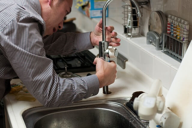 man troubleshooting a retractable faucet, leaning over with intense focus and vehemence