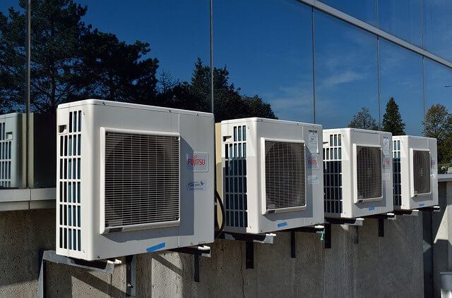 several hvac units with filters sitting outside on a concrete slab in front of a reflective glass 3-paned window wall