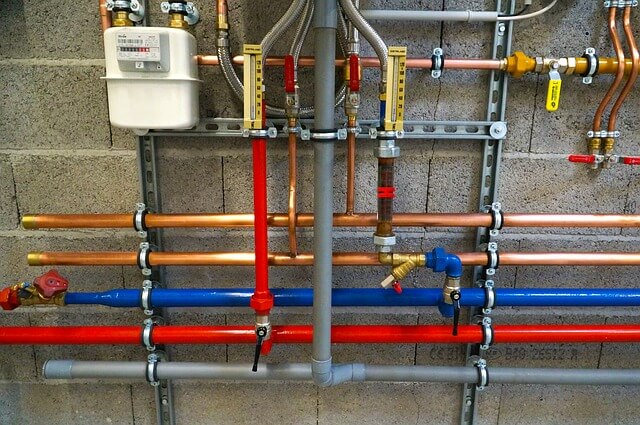 several multi-colored pex tubes organized mostly horizontally with a few bare metal pipes going upward on a concrete wall